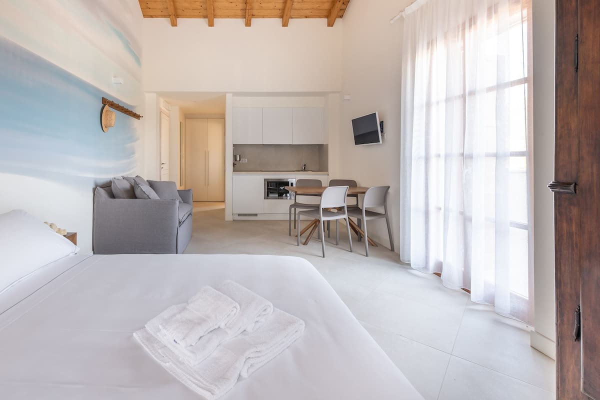 A modern hotel room with a bed, a sofa, a dining area, and a kitchen.