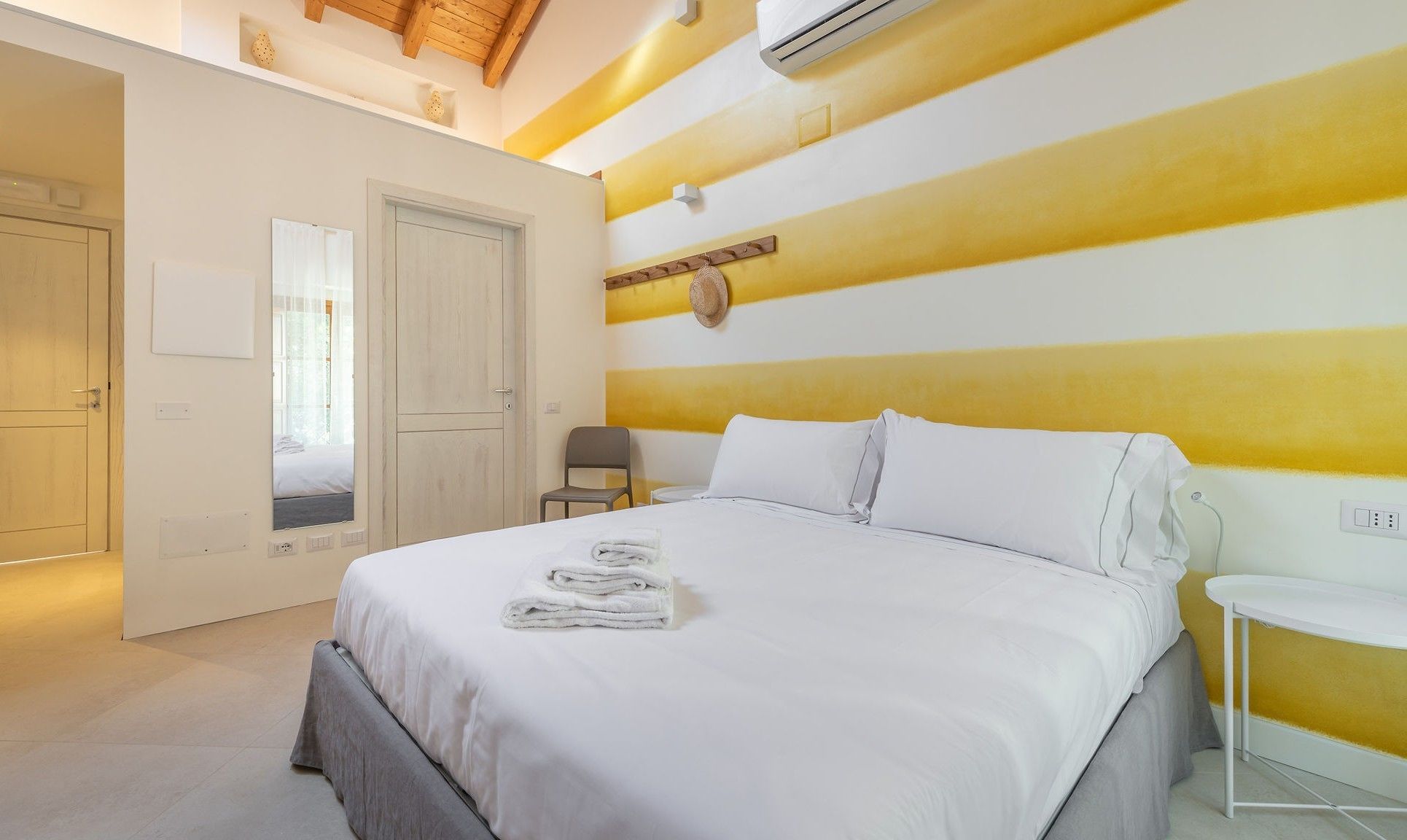 Habitación de hotel con cama, una silla, una mesita y aire acondicionado instalado en la pared.
