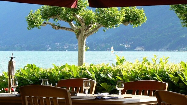 A table set for dining with a view of a lake and a sailboat in the distance. - Le Bel Abri (Annecy)
