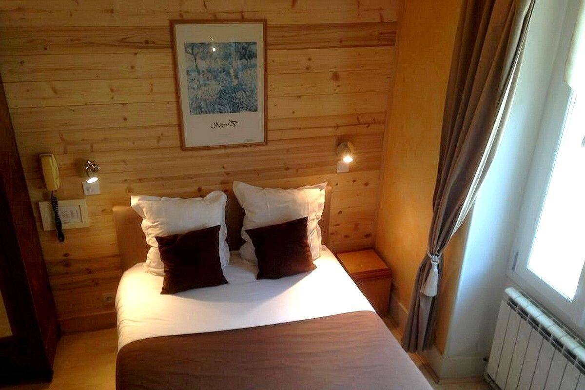 A wooden-paneled room with a bed, a framed picture on the wall, and a window with curtains.