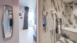A modern hotel room with a large mirror, a bed, a bathroom with marble walls, and a view of the outside. - Le Bel Abri (Annecy)