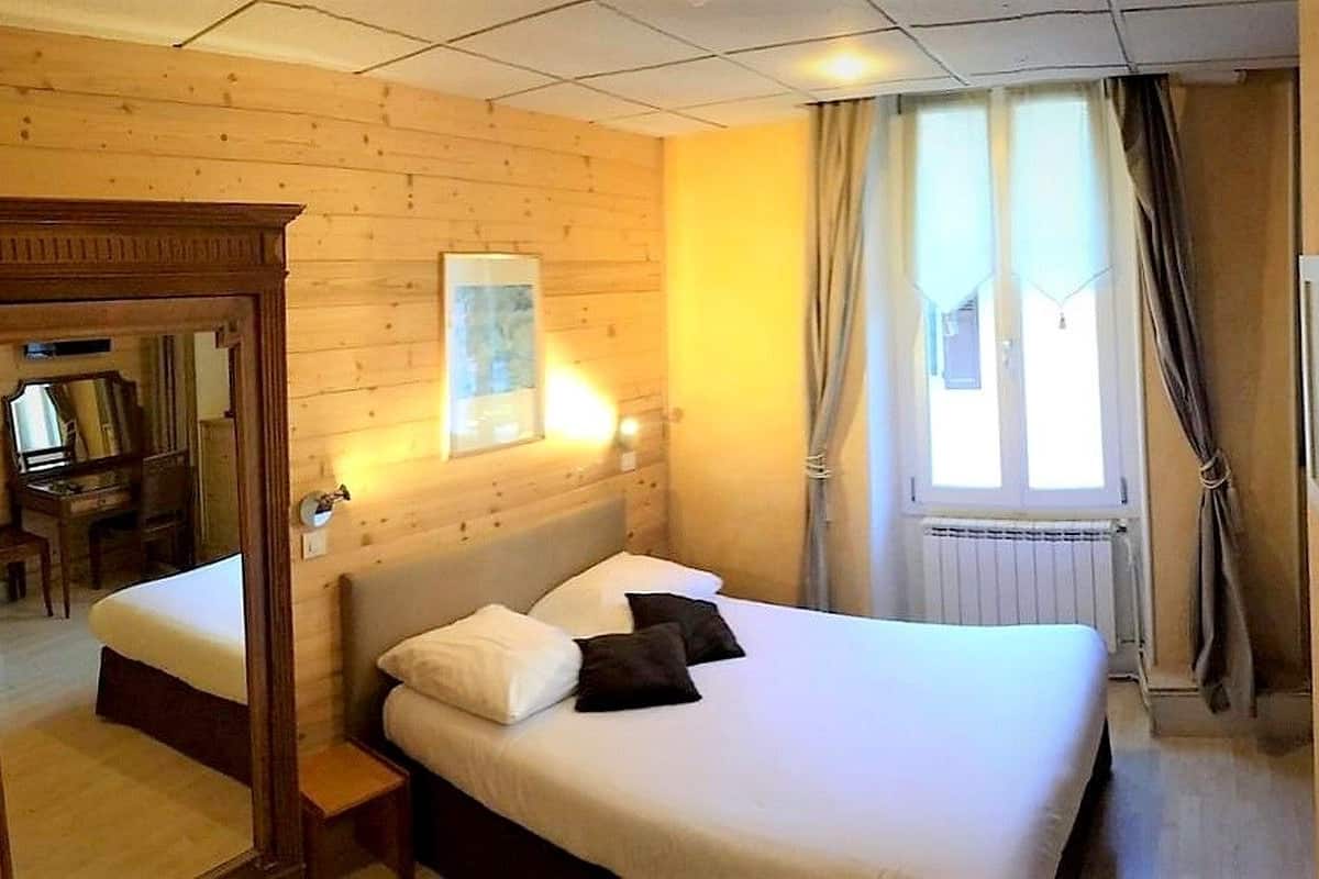 A hotel room with a wooden headboard, a bed with white bedding, a bedside table, a mirror, and a window with curtains.