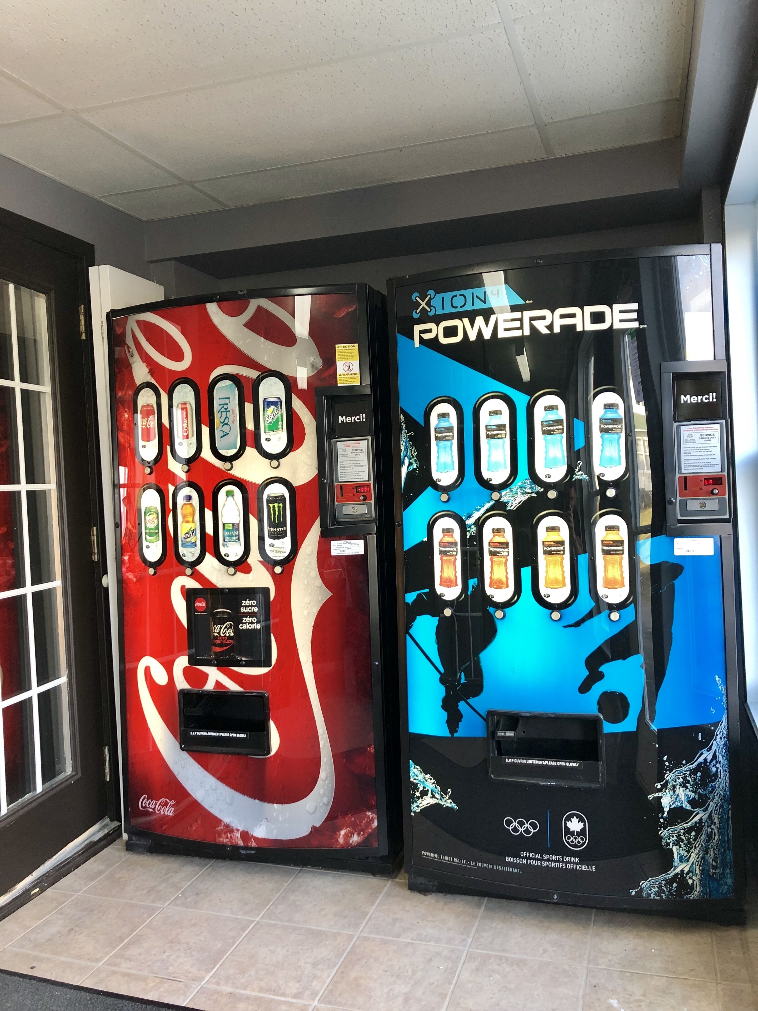 Two beverage vending machines, one branded with Coca-Cola and the other with Powerade, both with multiple drink options and payment interfaces.