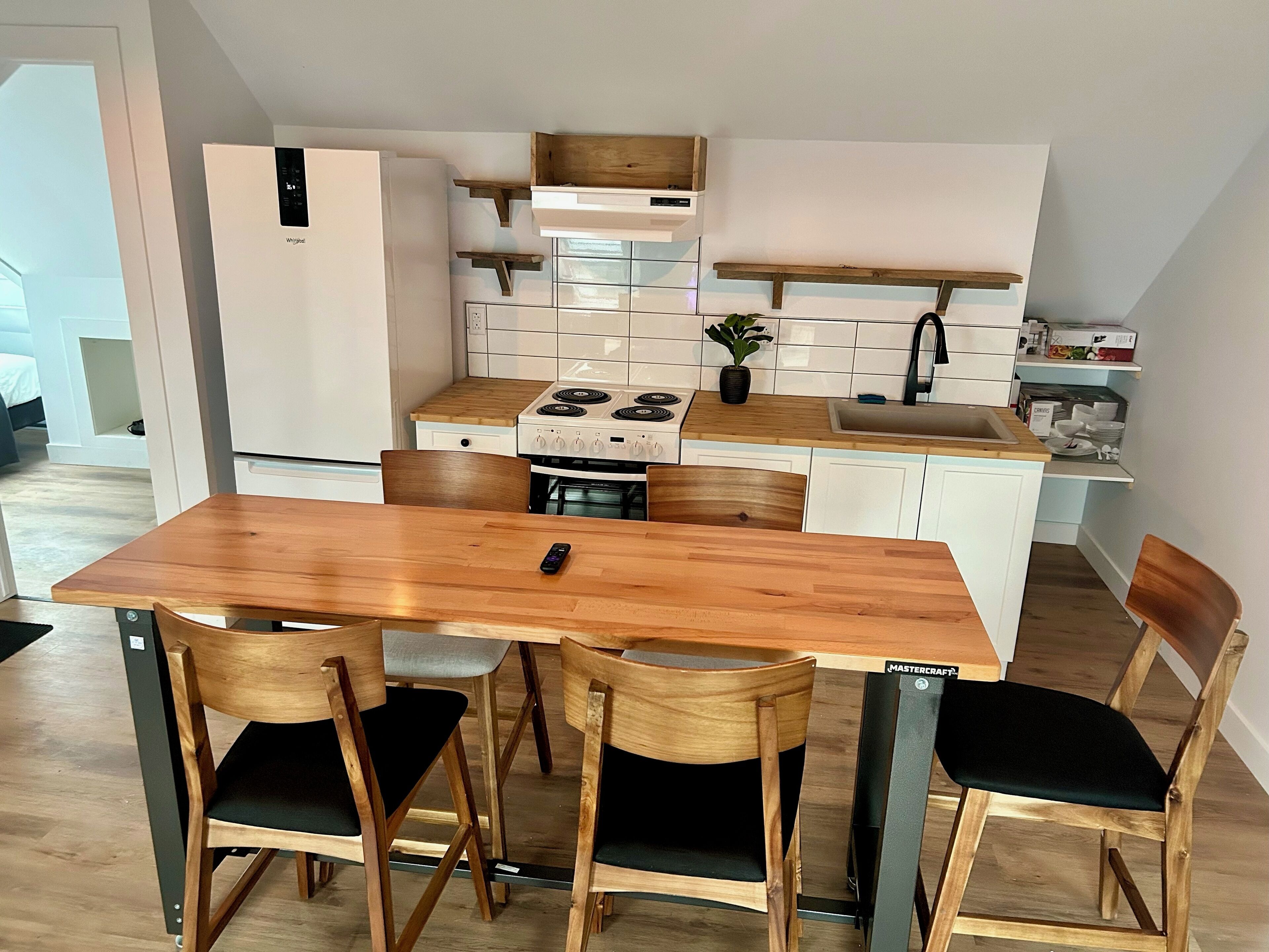 Cocina compacta con una mesa y sillas de madera, estufa y refrigerador.