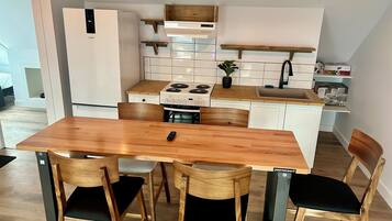 Cocina compacta con una mesa y sillas de madera, estufa y refrigerador.