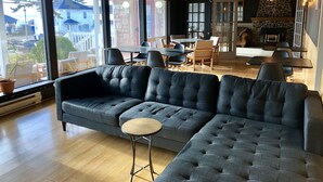 A modern living room with a sectional sofa, a small round table, and a dining area with chairs and a table. - Bleu Mer - hôtel & résidences (Carleton-sur-Mer)
