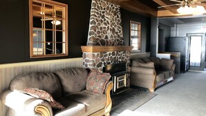 A living room with a stone fireplace, two sofas, and a television. - Bleu Mer - hôtel & résidences (Carleton-sur-Mer)