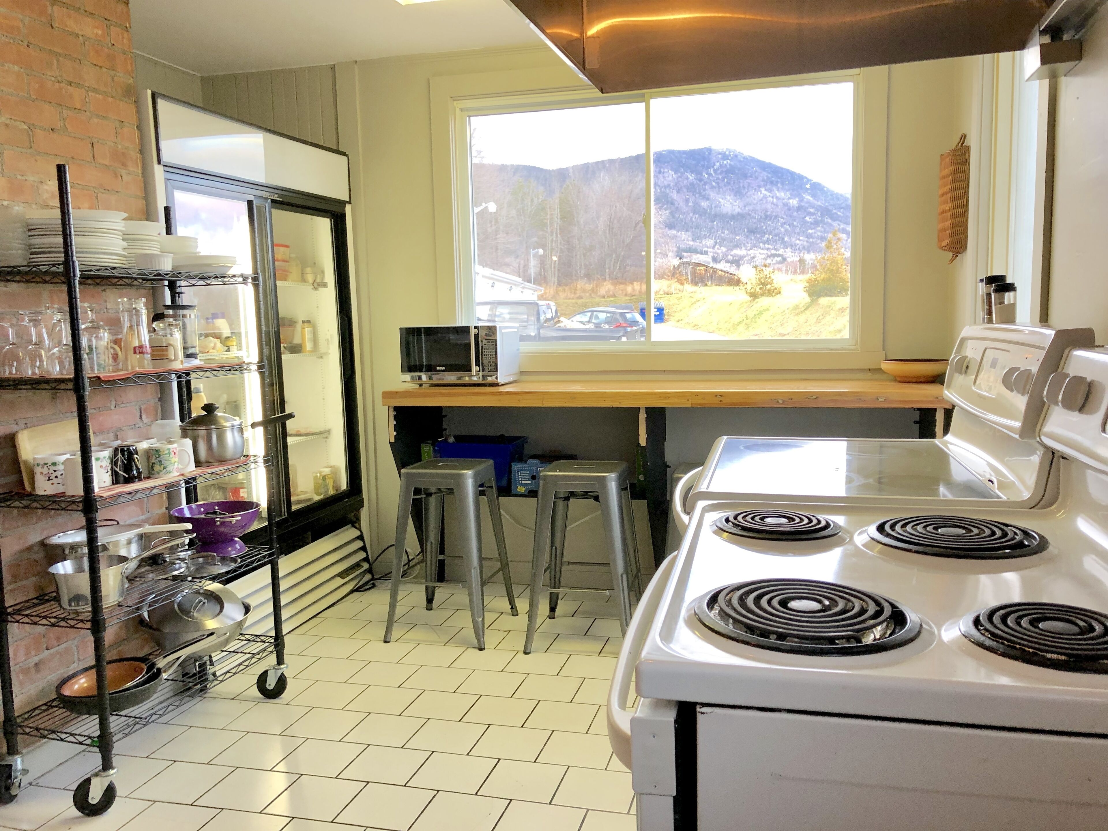 Una cocina con estufa, taburetes, refrigerador y ventana con vistas a la montaña.