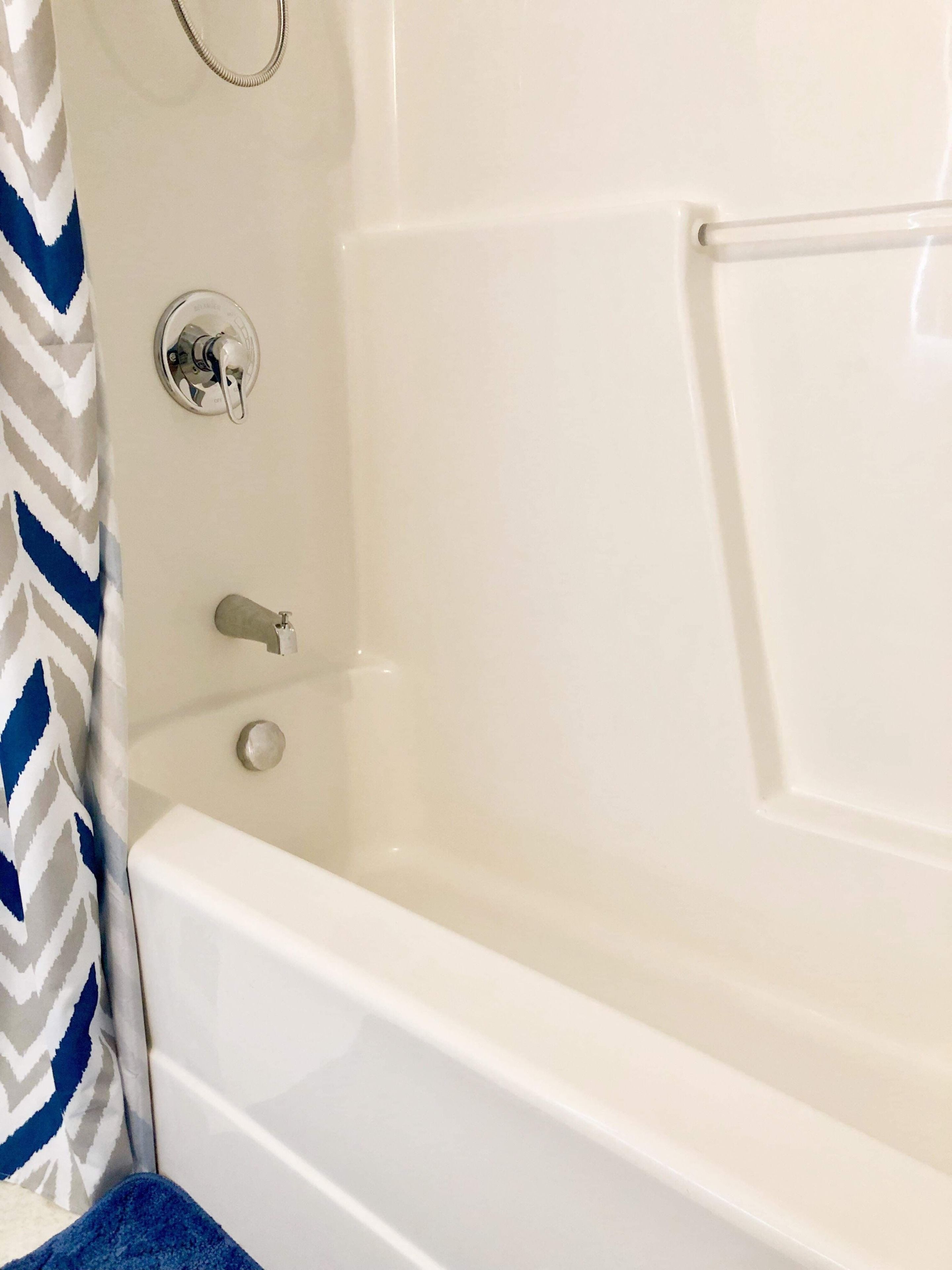Eine weiße Badewanne mit chromfarbenem Wasserhahn und Drehknopf, einem Handtuchhalter und einem Duschvorhang mit blau-weißem Fischgrätmuster.