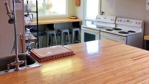 A kitchen with a wooden countertop, a stove, hanging pendant lights, and a window providing natural light. - Bleu Mer - hôtel & résidences (Carleton-sur-Mer)
