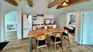 A modern kitchen with wooden beams, a dining table with four chairs, and pendant lighting. - Bleu Mer - hôtel & résidences (Carleton-sur-Mer)