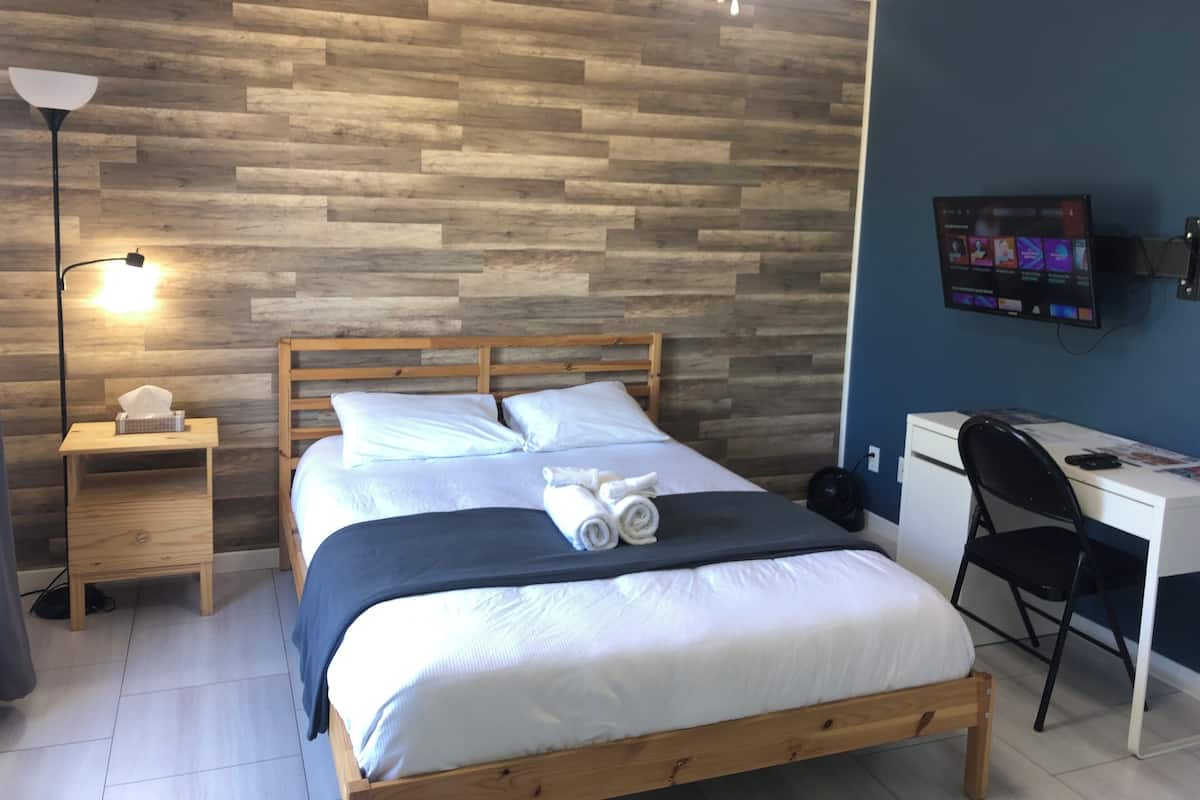 Un dormitorio ordenado con una cama de madera, un escritorio, una silla, un televisor y una lámpara de noche.