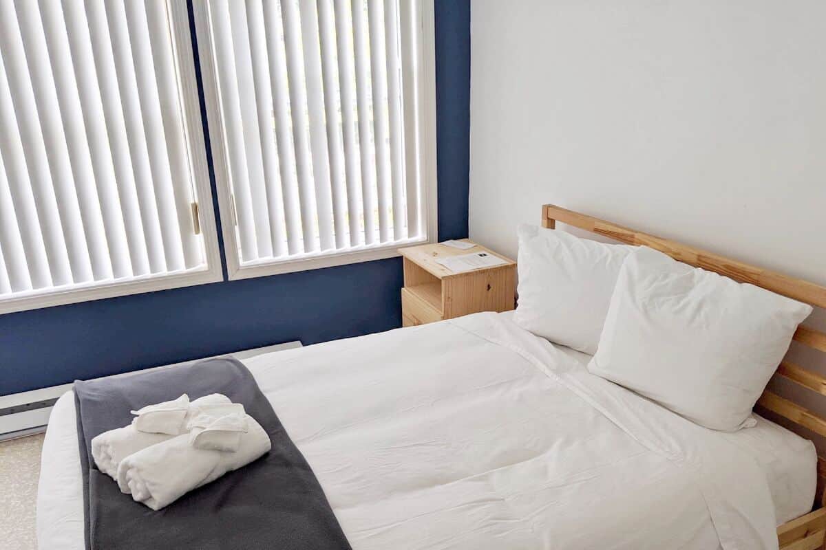 Una cama bien hecha con sábanas blancas, un cabecero de madera y una mesita de noche de madera con una lámpara.