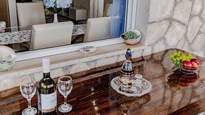 Ein Essbereich mit Steinwand, Holztisch und Spiegel, der den Raum reflektiert. Es sind Weingläser, eine Flasche und ein dekorativer Tablett mit Kerze und Obstschale vorhanden.