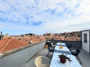 Una terraza en la azotea con una mesa, sillas, una planta en maceta y vistas de un paisaje urbano con tejados de terracota y edificios históricos.