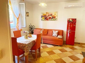 Un coin repas avec une table dressée pour deux personnes, un canapé et un réfrigérateur rouge.
