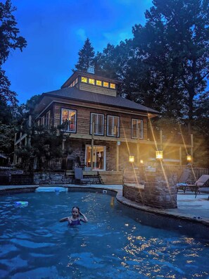 Uma casa de madeira de dois andares com piscina, rodeada por árvores.