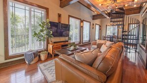 A spacious living room with a large leather sofa, a flat-screen TV, and a wooden staircase.