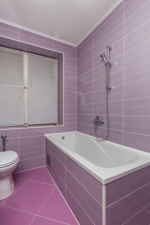 A bathroom with purple tiles, a white bathtub, and a toilet. - Apartments Sany - One Bedroom Apartment with Balcony and Sea View (Cavtat)