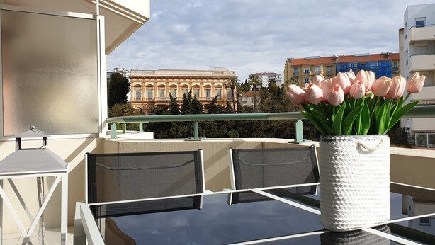 Un balcon avec une table, des chaises et un vase rempli de tulipes roses.