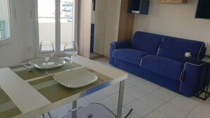 Un salon moderne avec un canapé bleu, une table à manger avec un plateau en verre et un balcon offrant une vue.