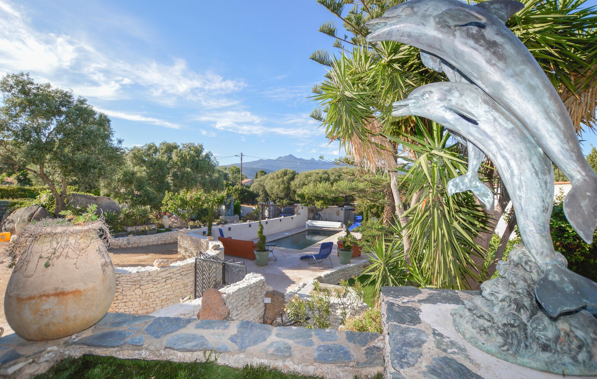 Zona de piscina amb parets de pedra, una escultures decorativa gran i vistes a les muntanyes al fons.