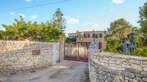 Ingresso in pietra a un edificio con un cancello in metallo, un muro di pietra con un cartello e uno stabile con tetto in tegole sullo sfondo.