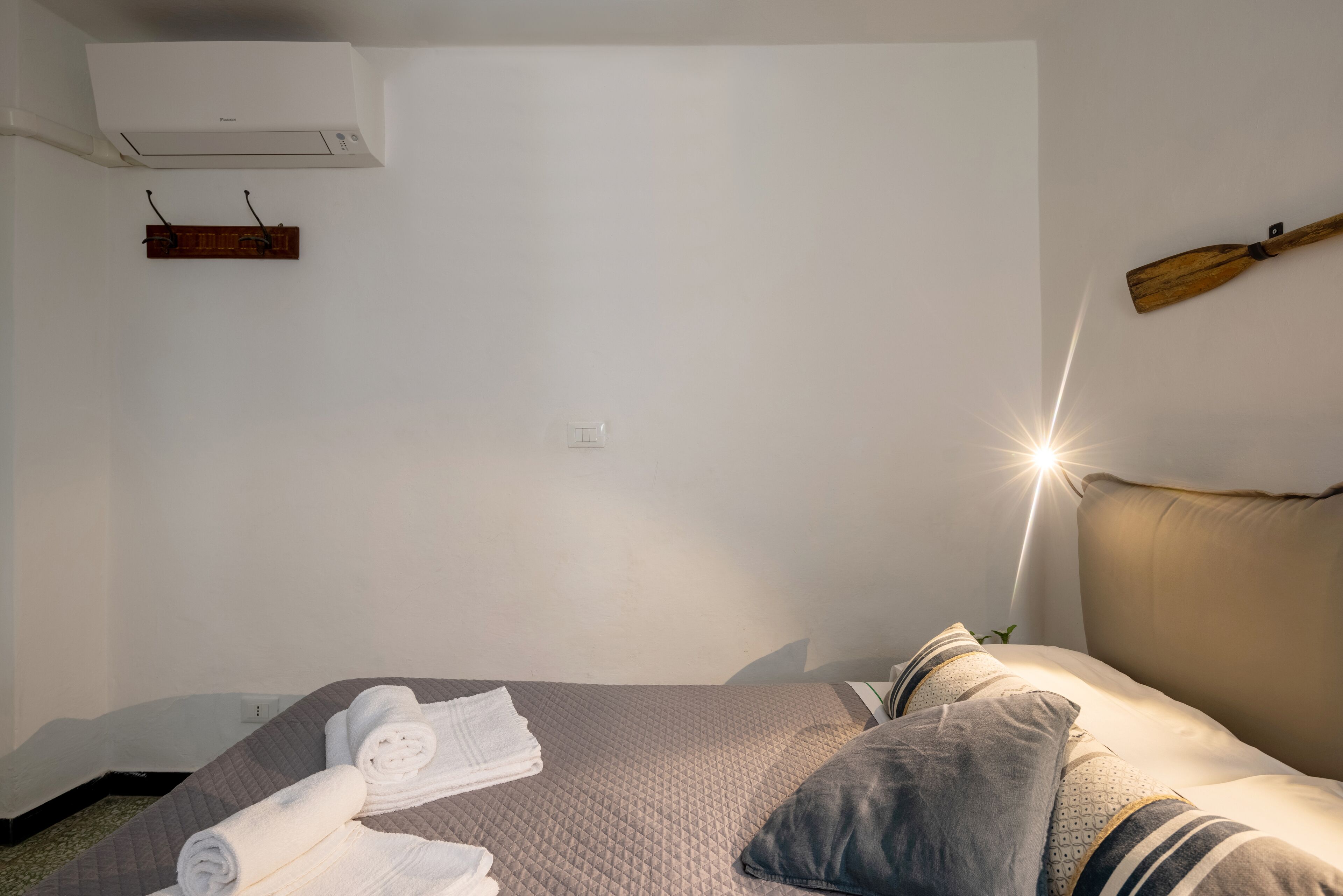 A hotel room with a bed, towels, a wooden headboard, and a wall-mounted air conditioner.