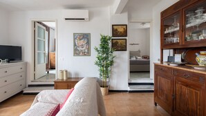 Een woonkamer met een bank, een televisie, een kast met glazen deuren, een plant en een schilderij aan de muur.