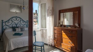 Een slaapkamer met een bed, een dressoir, een stoel en een raam met gordijnen.