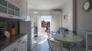 Een keuken met witte kasten, een ronde tafel en uitzicht op gebouwen.