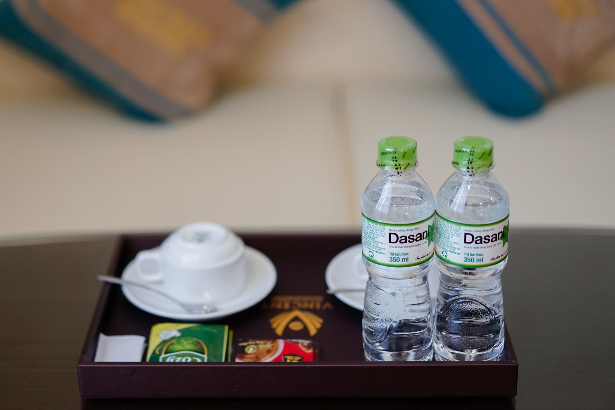 A tray with two Dasani water bottles, a white teapot, and two teacups on a table.