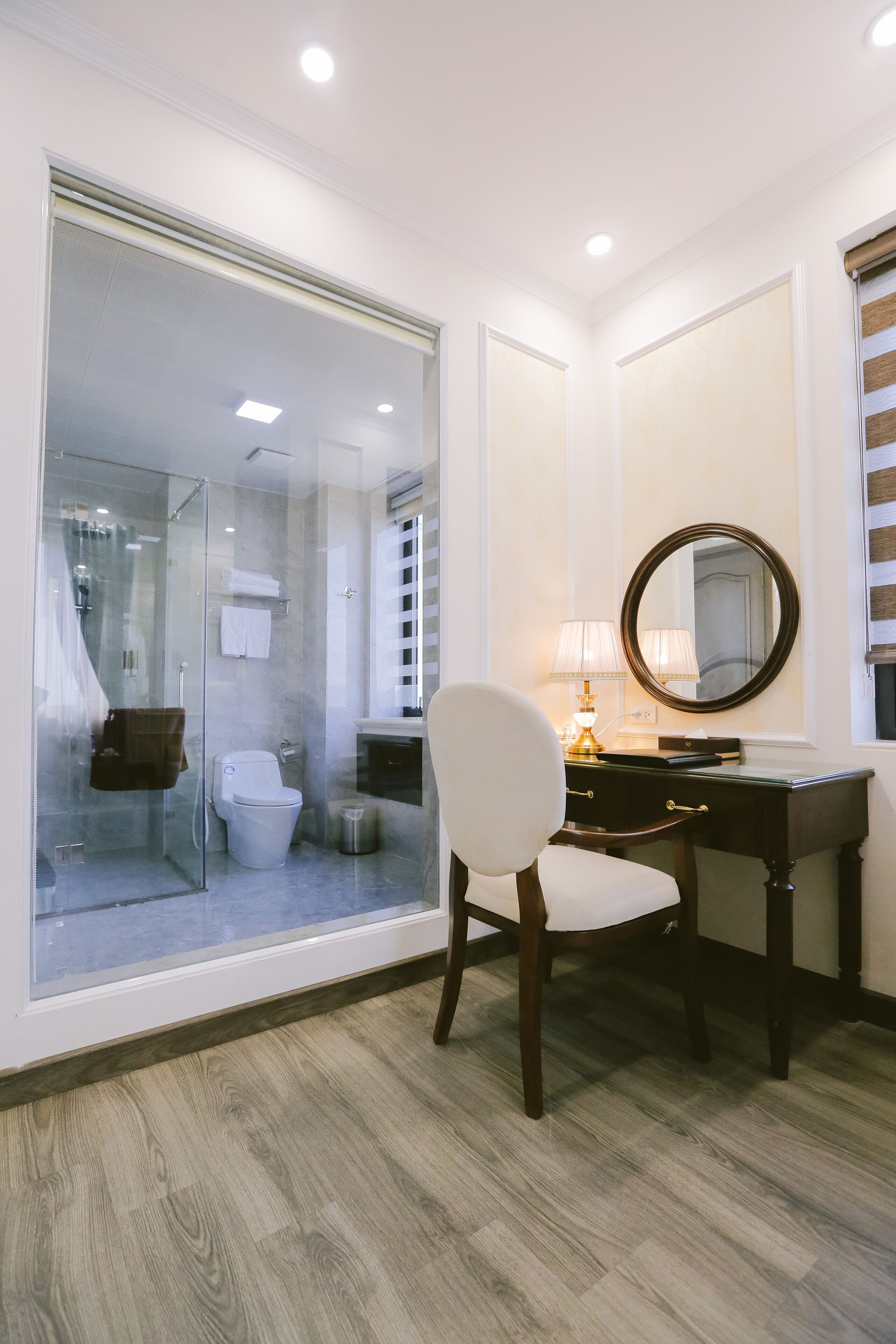 Un baño moderno con cabina de ducha de vidrio, inodoro blanco, tocador con espejo y una silla.