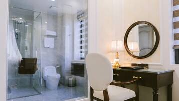 Un baño moderno con cabina de ducha de vidrio, inodoro blanco, tocador con espejo y una silla.