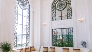 A spacious living room with a large white sofa, a glass coffee table, and two large arched windows with metal grilles. - Vincent Halong Hotel (Bai Chay)