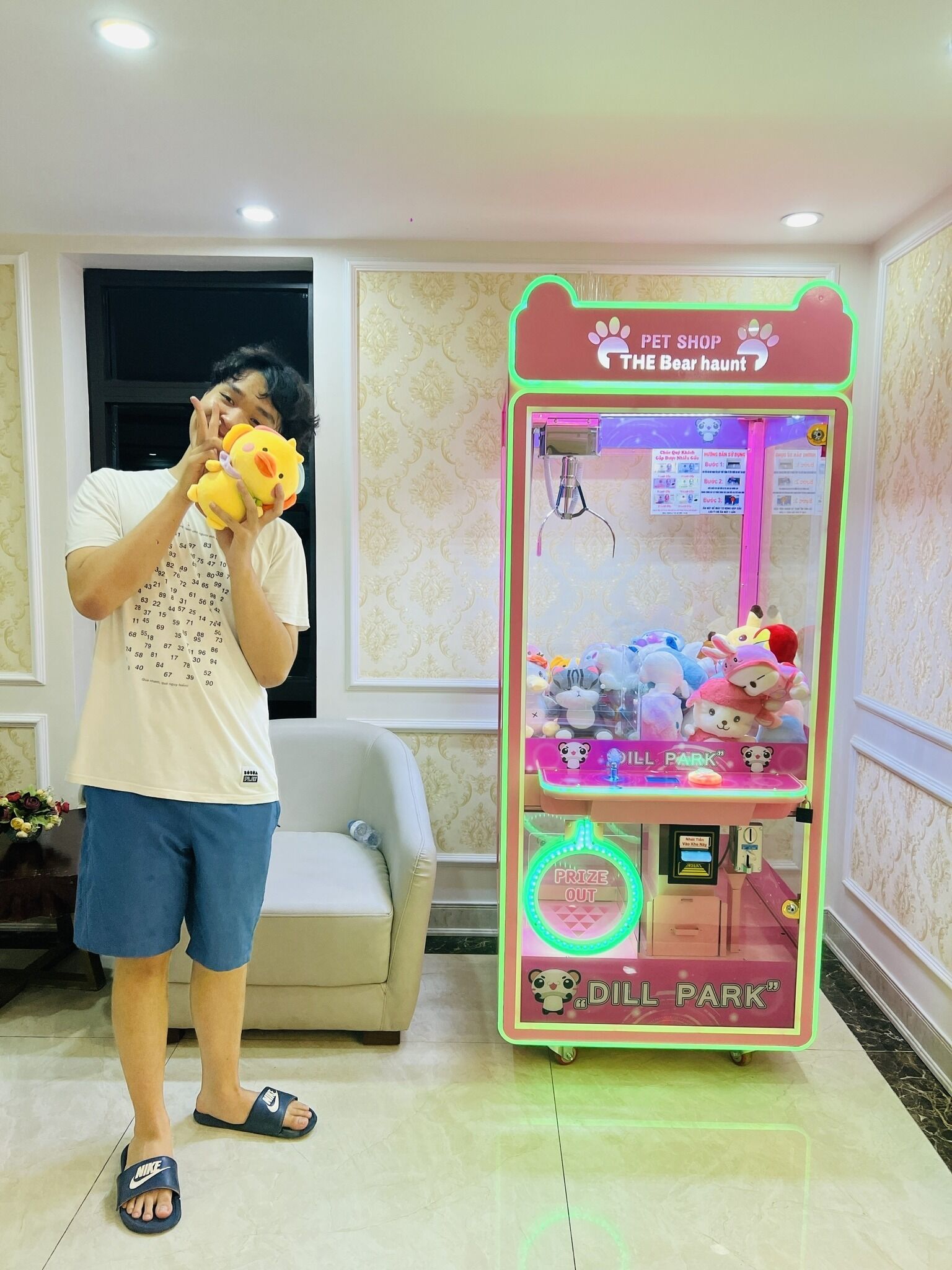 A person playing a claw machine game in a room with a patterned wallpaper and a sofa.