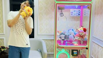 A person playing a claw machine game in a room with a patterned wallpaper and a sofa.