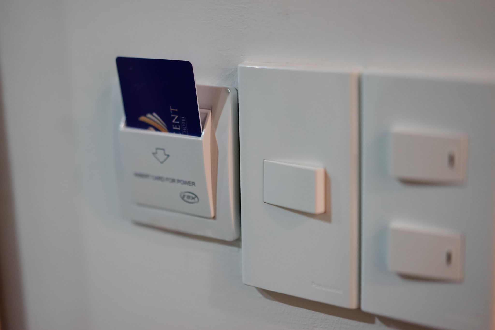 Un lector de tarjetas instalado en la pared, con una tarjeta insertada, junto a un interruptor de luz y un enchufe.