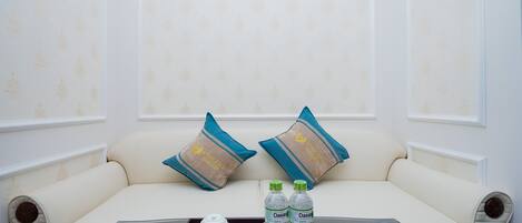 Un sofá con dos almohadones decorativos, una bandeja con tetera, tazas, agua embotellada y una caja de bombones.