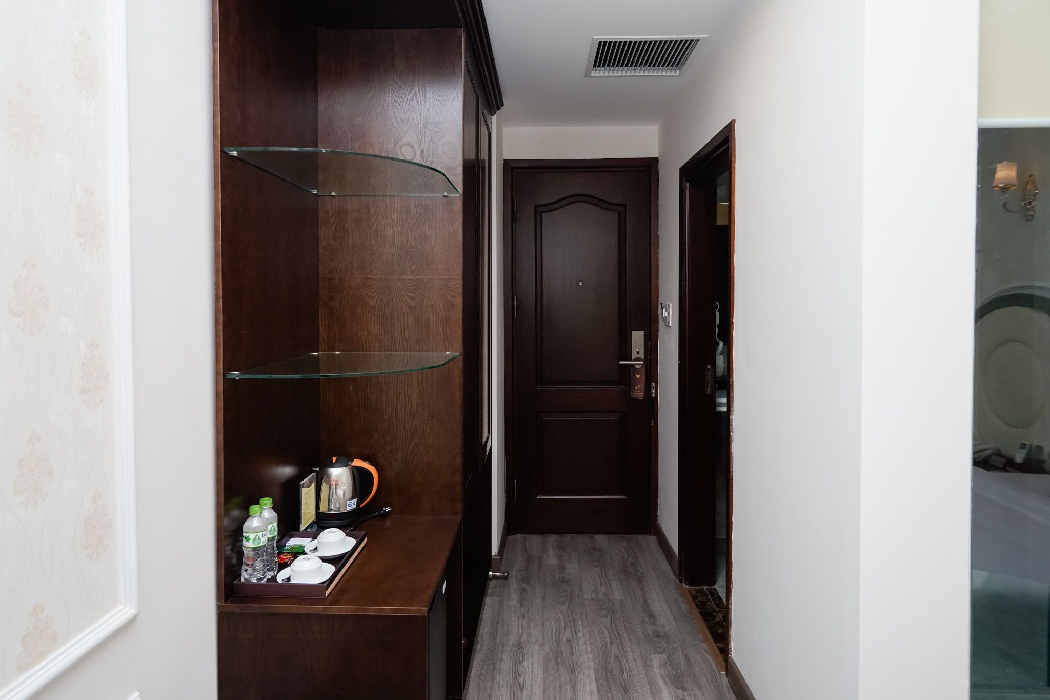 Un couloir avec une armoire en bois, une étagère en verre et un plateau contenant des articles de toilette.