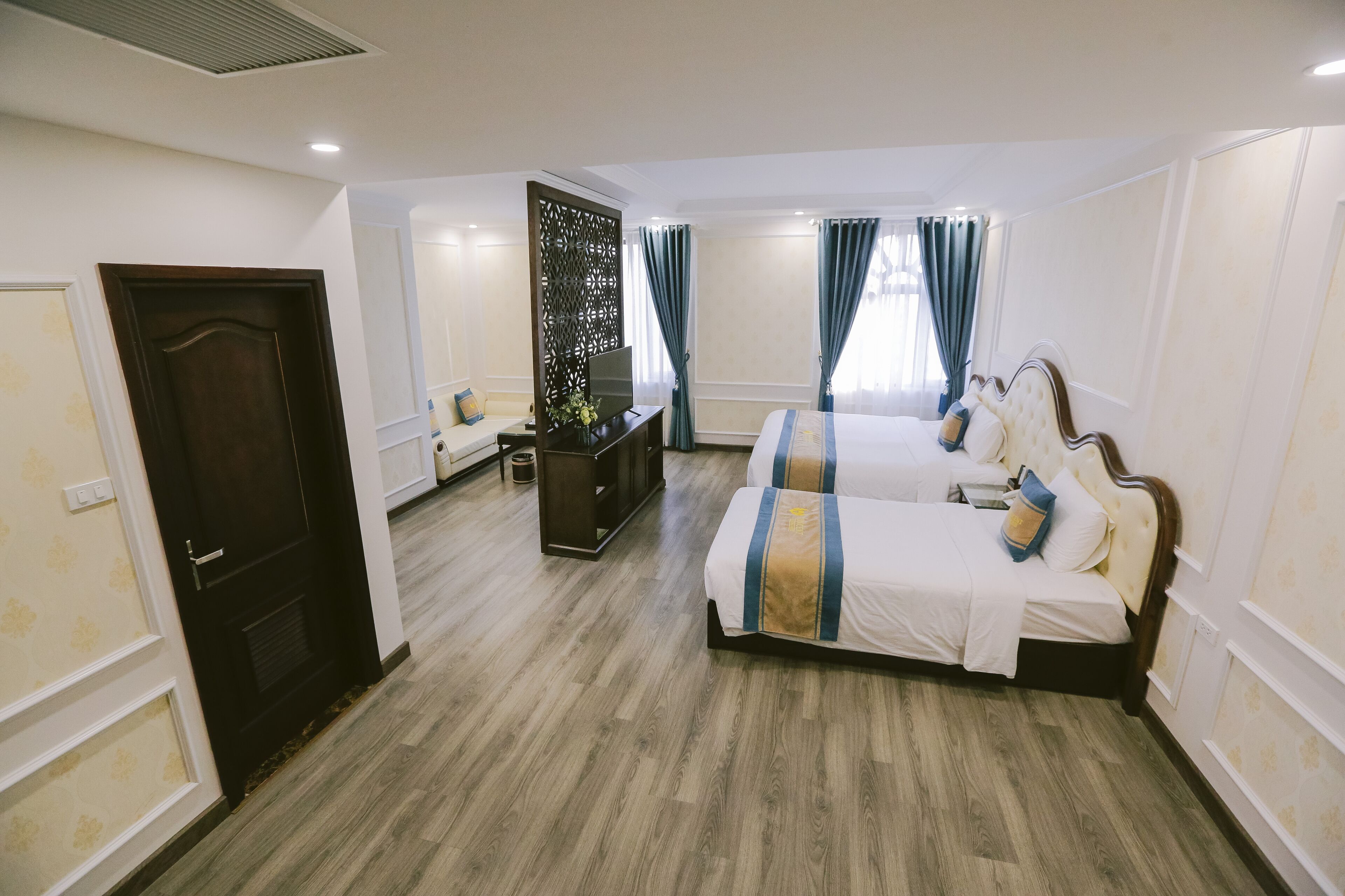 Habitación de hotel con dos camas, televisor, escritorio y un separador decorativo.