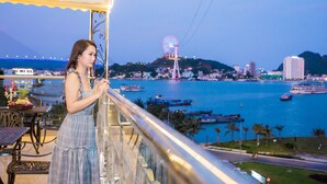 A balcony with a view of a waterfront cityscape, including boats and a Ferris wheel. - Vincent Halong Hotel (Bai Chay)