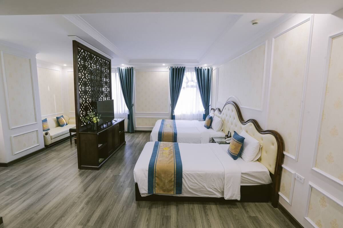 A hotel room with two beds, a TV, a sofa, and a decorative screen.