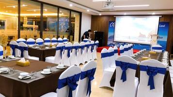 A conference room with rows of white chairs with blue sashes, tables set for a meeting, a projector screen, and a presentation area.