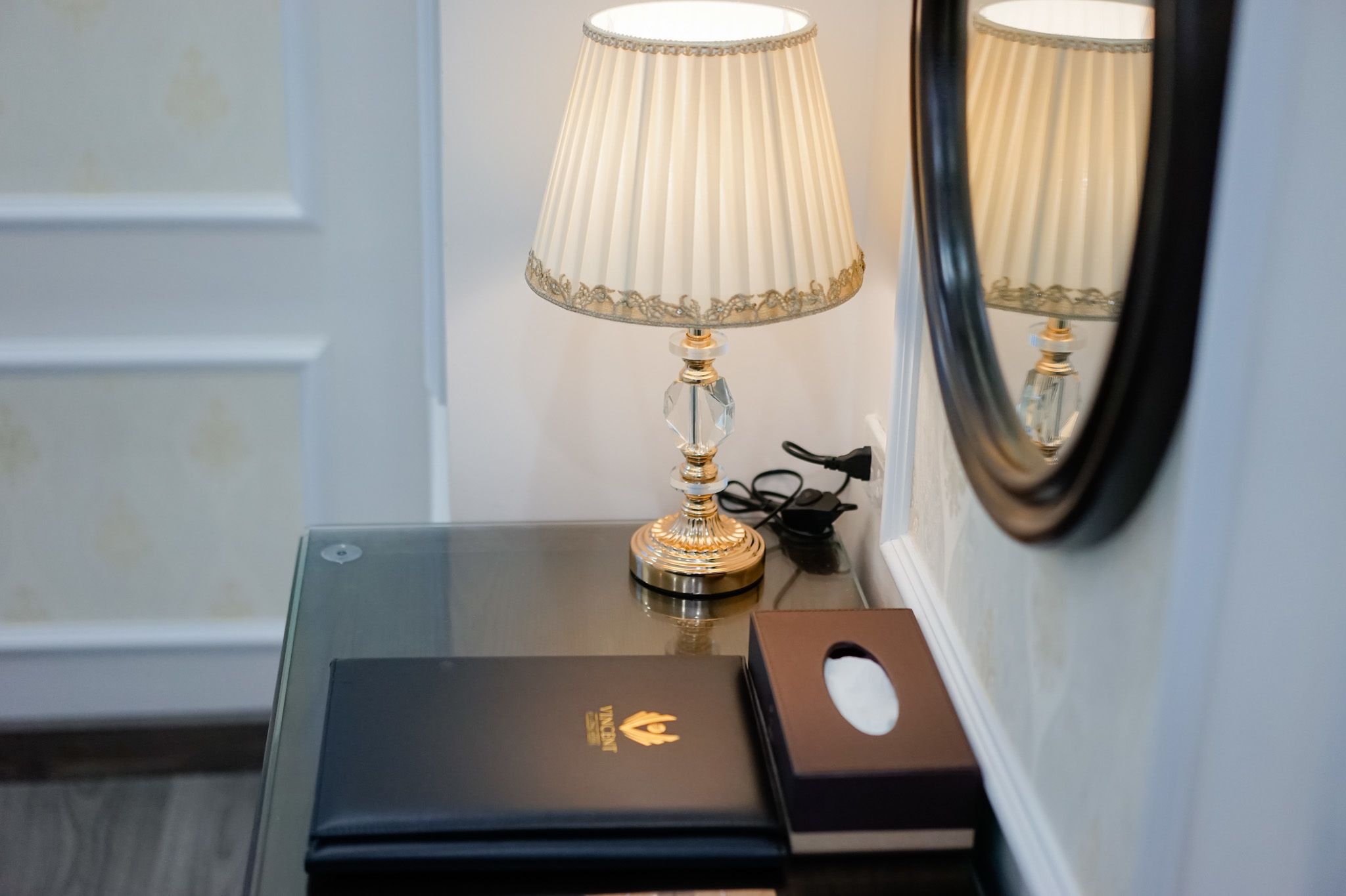 Une chambre d’hôtel avec une lampe de table, un miroir et un boîtier noir orné d’un emblème doré.
