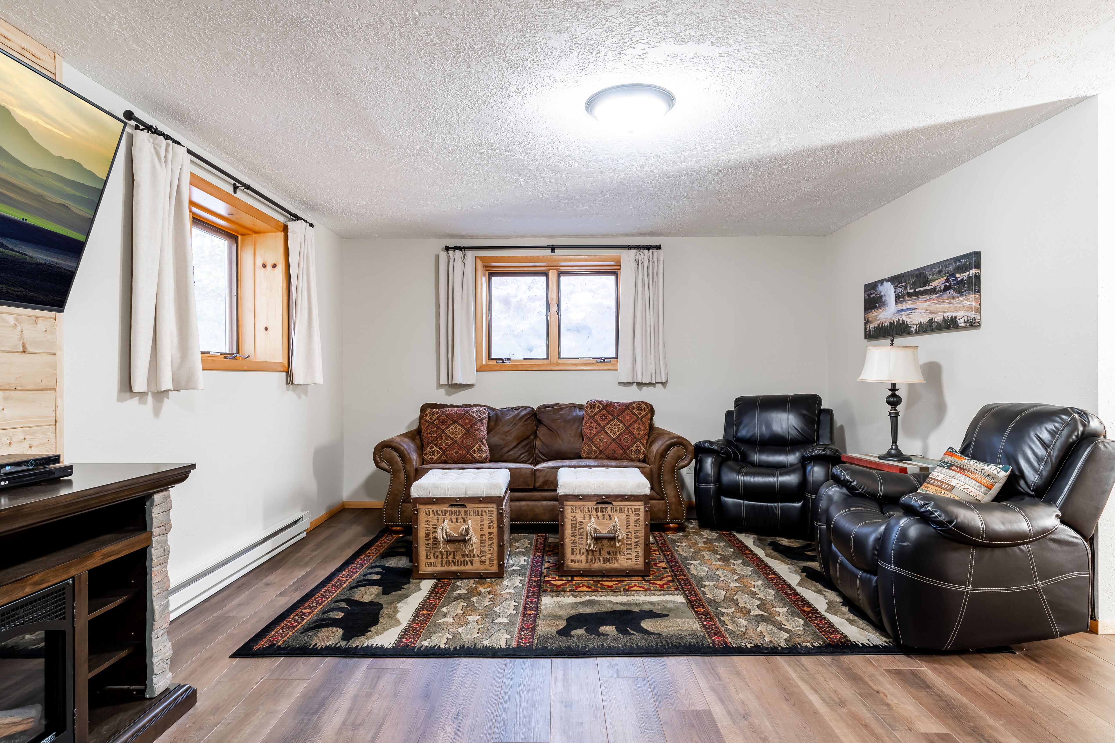 A living room with a brown leather sofa, two ottomans, a black leather armchair, a wooden coffee table, and a patterned rug.