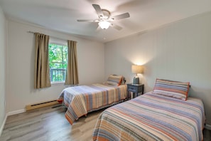 Ein Schlafzimmer mit zwei Betten, einem Deckenventilator, einem Fenster mit Vorhängen und einem Nachttisch mit Lampe.