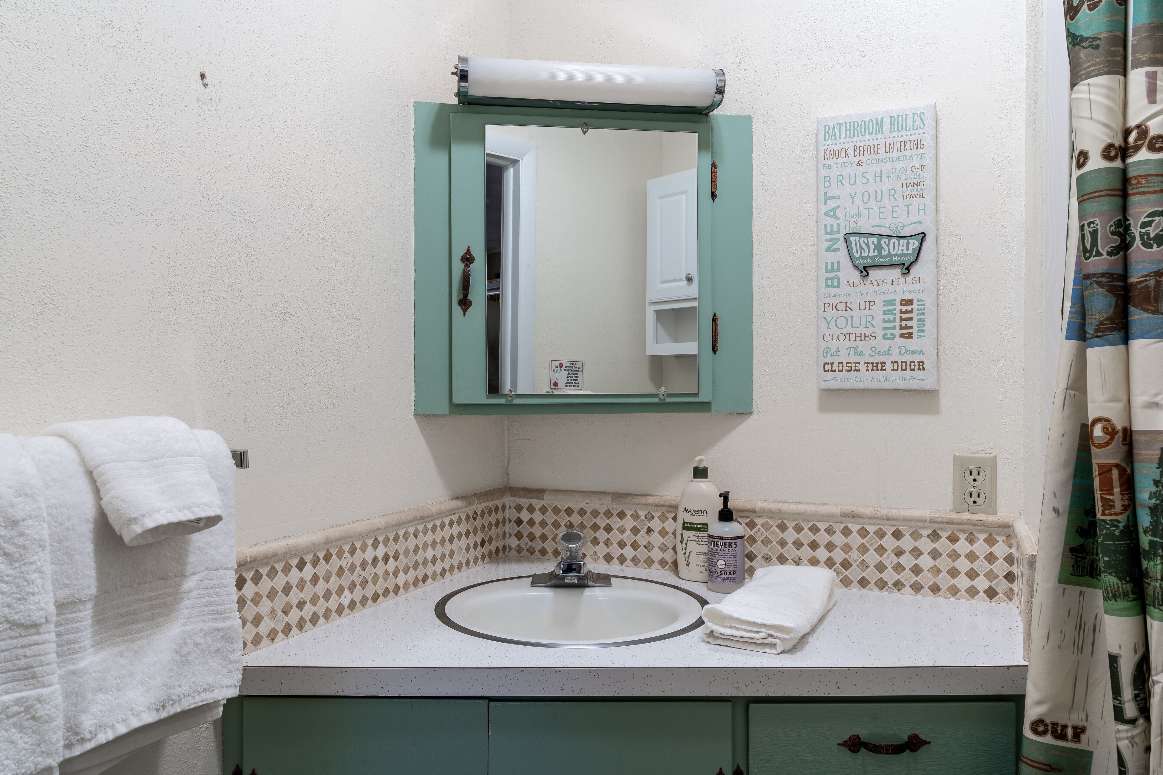 A bathroom with a green vanity, a sink, a mirror, and a poster with bathroom rules.