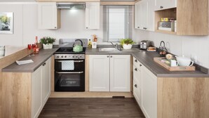 Een moderne keuken met witte kastjes, een zwarte oven, een groene waterkoker en een houten aanrecht.
