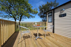 A wooden deck with a table and two chairs, a sign reading "BURGUNDY," and a clear blue sky. - Polborder Holidays (Looe)